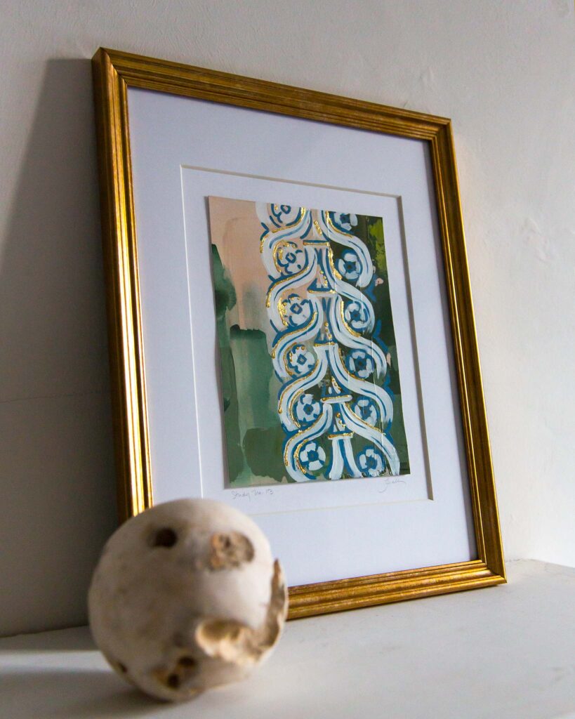 Angled view of Teale Hatheway’s Forma Coloris Lux Mentis — Study No. 13 framed in gold with a double mat, resting on a white mantel. The image highlights the gilded detailing within the scrolling blue-and-white architectural patterns, with abstract green and peach backgrounds and a textured stone sphere in the foreground.