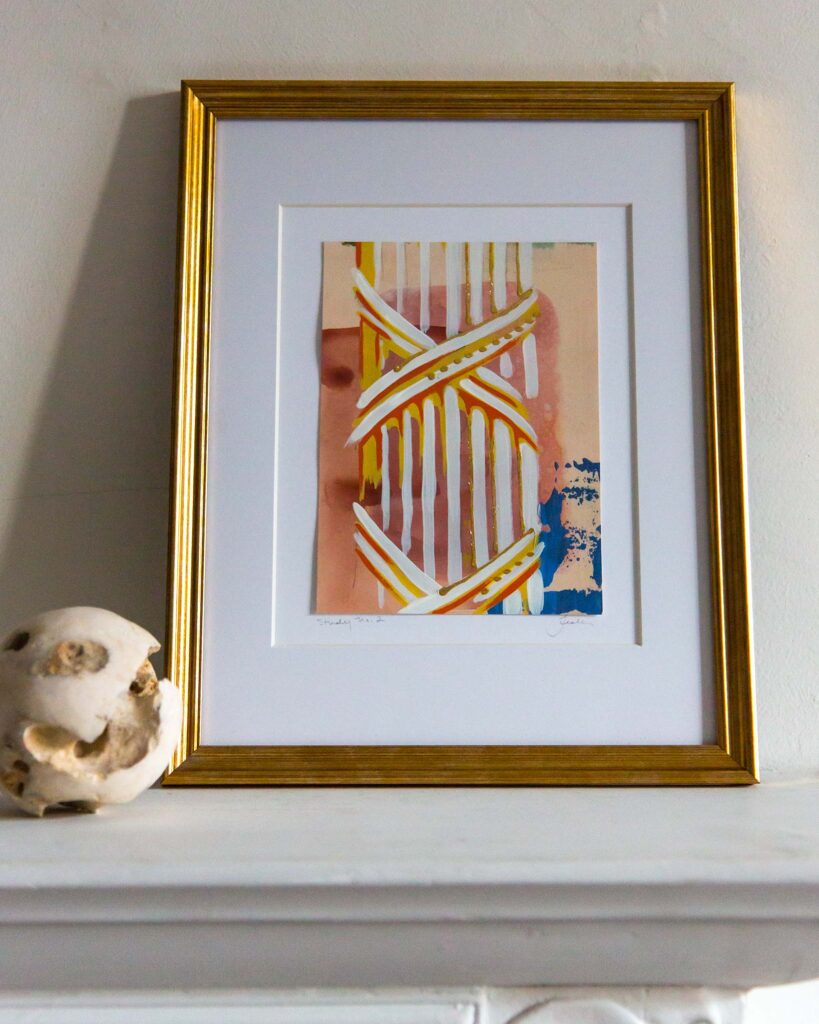Framed architectural study painting, Forma Coloris Lux Mentis — Study No. 2 by Teale Hatheway, displayed on a white mantel in a gold frame with a double mat. The artwork’s warm palette and hand-gilded details glow softly beside a sculptural stone sphere.
