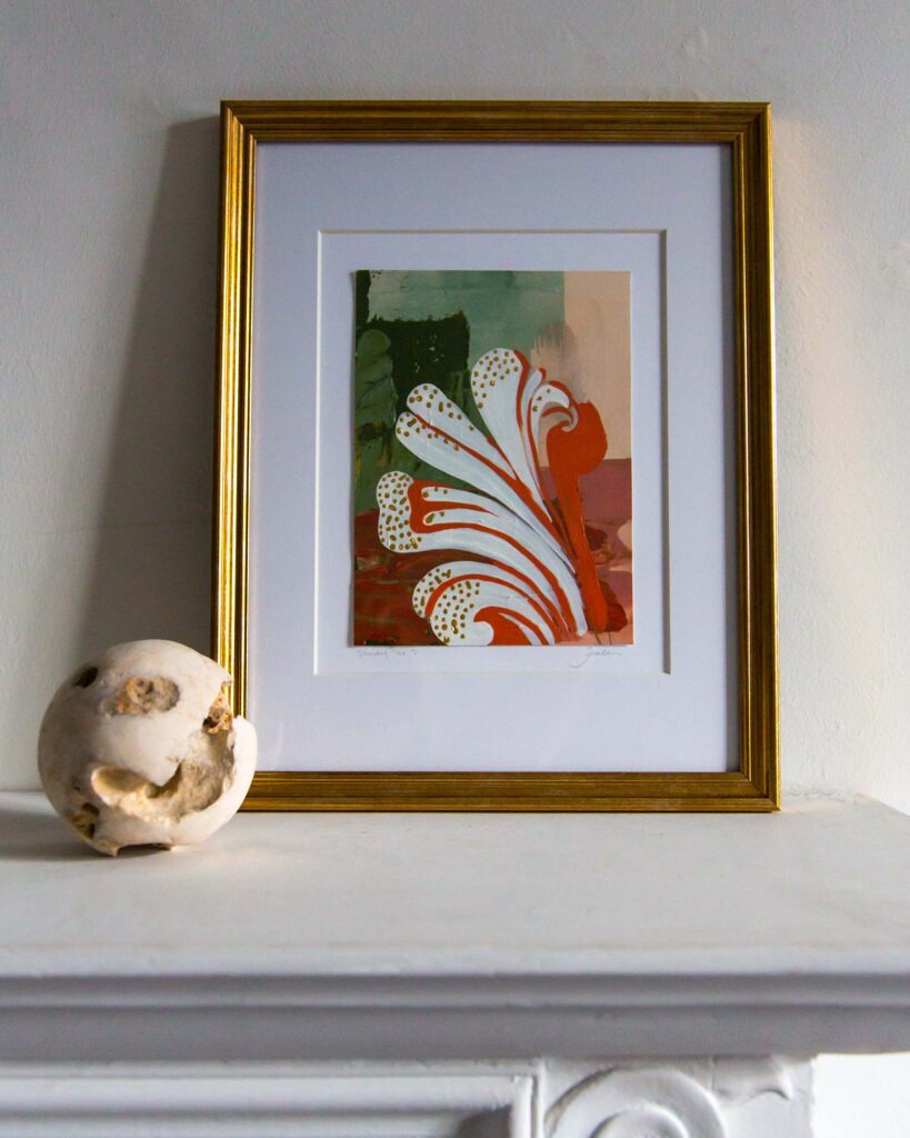 Framed architectural painting, Forma Coloris Lux Mentis — Study No. 3 by Teale Hatheway, displayed on a white mantel in a gold frame with a double mat. The artwork features a dynamic, curling motif accented with gilded details, paired with a textured stone sphere for scale.