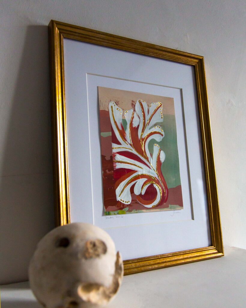 Angled view of Teale Hatheway’s Forma Coloris Lux Mentis — Study No. 6 framed in gold with a double mat, resting on a white mantel. The photograph highlights the dimensional gilding and curving architectural motif, with a textured stone sphere in the foreground.