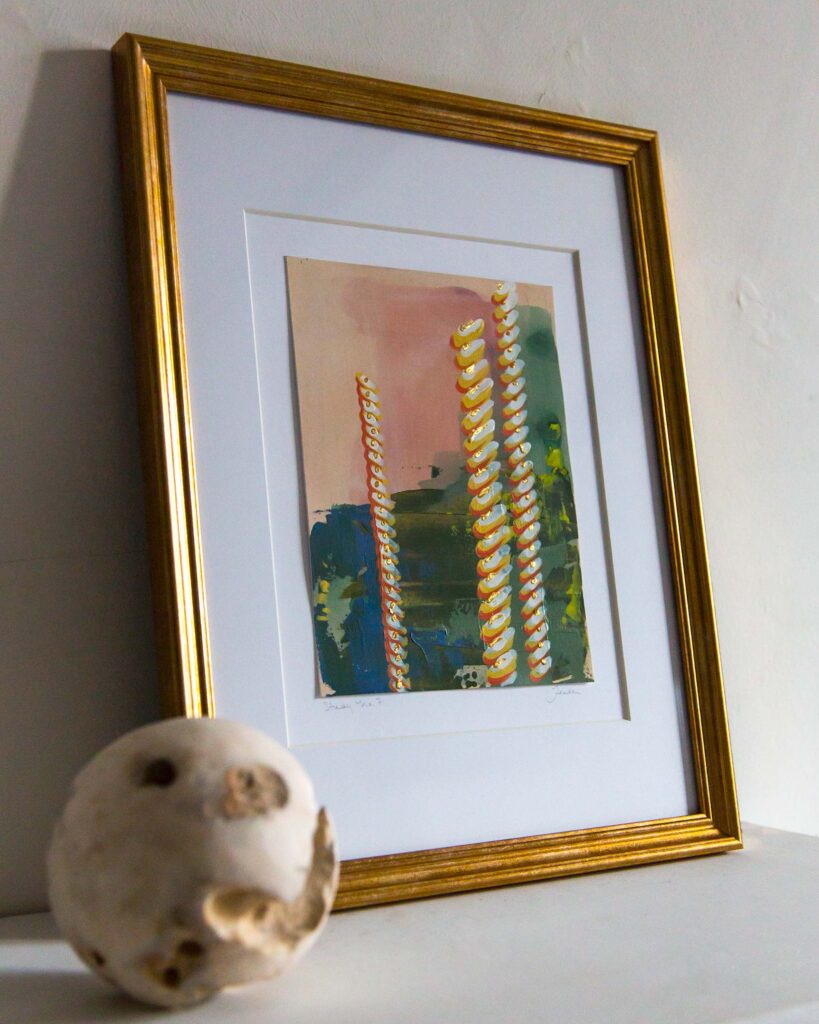 Angled view of Teale Hatheway’s Forma Coloris Lux Mentis — Study No. 7 framed in gold with a double mat, resting on a white mantel. The photograph highlights the spiraling, gilded architectural motifs and textured color fields, with a stone sphere in the foreground.